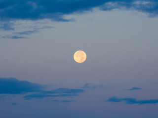 Full moon against brightening dawn sky and blue clouds
