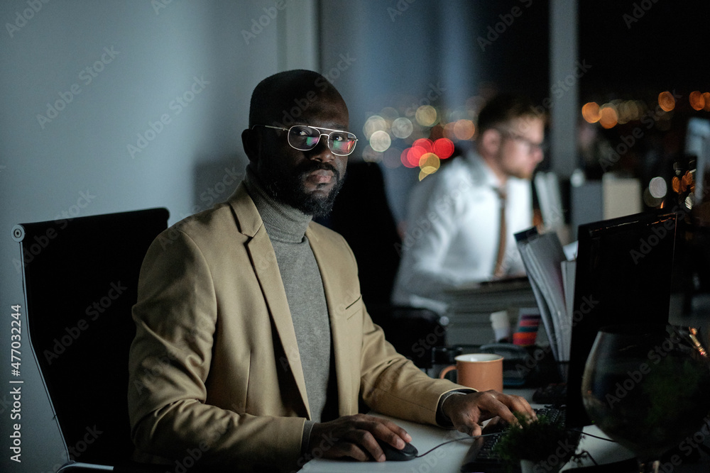 Poster young african broker in formalwear sitting in front of computer while analyzing financial data in of