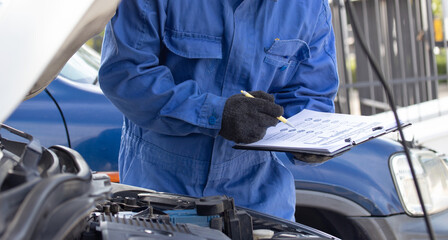 Portrait of a mechanic at work in his garage auto check up and car service shop concept. Mechanic writing job checklist to clipboard at workshop garage.