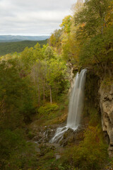 A mountain waterfall cascades over boulders with trees in full autumn seasonal color