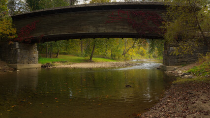 Autumn color reflects of the water beneath a wooden covered bridge in rural Virginia