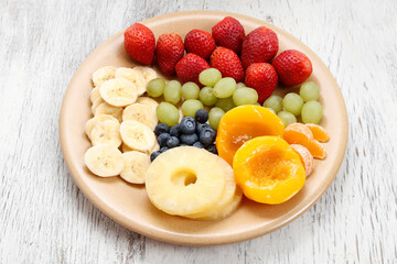 Plate with fruits: bananas, strawberries, grapes, blueberries, pineapple, peach and orange.