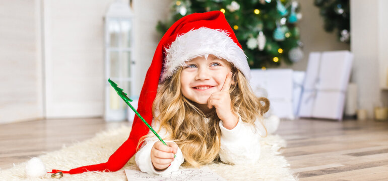 Little girl in Santa hat writes letter to Santa Claus