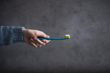 Woman hand holding a toothbrush on the dark, concrete background. Dental care.