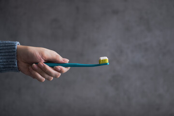 Woman hand holding a toothbrush on the dark, concrete background. Dental care.