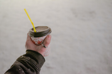 a glass with a hot drink in the hand of a young man against a background of snow