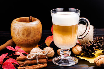 Glass cup of coffee latte and cinnamon sticks on a background of autumn leaves