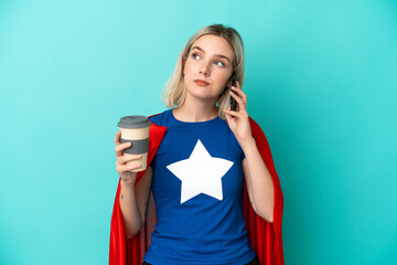 Naklejka premium Super Hero caucasian woman isolated on blue background holding coffee to take away and a mobile