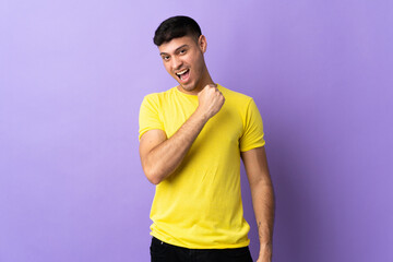 Young Colombian man isolated on purple background celebrating a victory