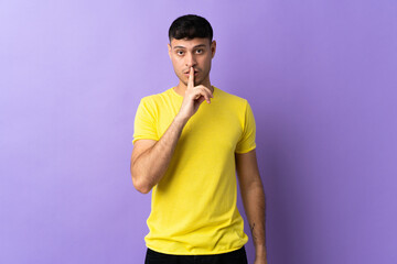 Young Colombian man isolated on purple background showing a sign of silence gesture putting finger...