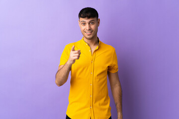 Young Colombian man isolated on purple background surprised and pointing front