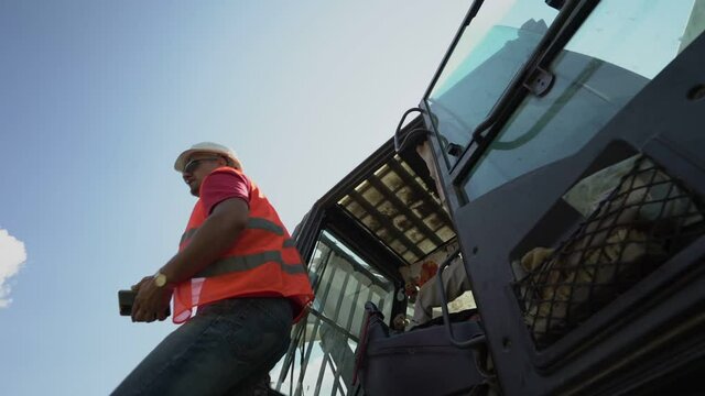 driver excavator in sunglasses and construction helmet finishes work and leaves excavator cabin outdoors