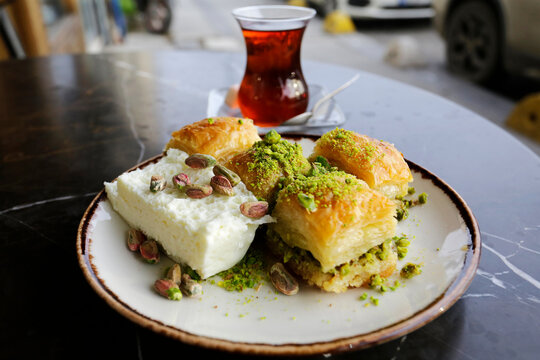 Baklava is seen served with a lot of pistachios and Kaymak clotted cream in a pastry shop of Istanbul, Turkey, backgrounded by the traditional Turkish tea.
