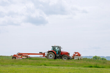 A red tractor mows the grass on a farmer's field. Two mowers will mow a large area of the field.