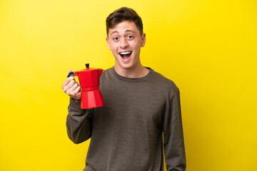 Young Brazilian man holding coffee pot isolated on yellow background with surprise facial expression