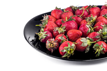 Fresh strawberry on black ceramic plate on white background. Summer fruit. Close up image with copy space.