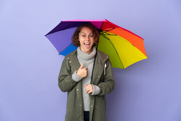 English woman holding an umbrella isolated on purple background with surprise facial expression