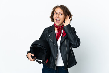 English woman holding a motorcycle helmet isolated on white background listening to something by putting hand on the ear