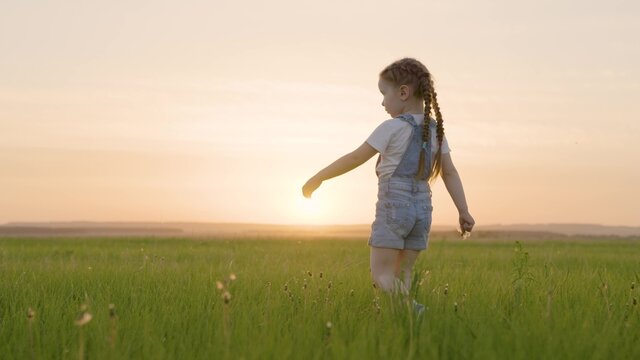 Happy child, girl walks on green grass in spring park. Kid walks outdoors in summer. Healthy outdoor games for children. A childhood dream. Happy family, childhood. Child having fun in the meadow