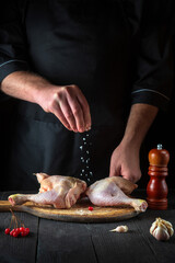 Professional chef prepares raw chicken legs in the restaurant kitchen. The cook adds salt to the chicken leg before baking. National dish
