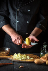 Obraz na płótnie Canvas Professional chef cuts raw potatoes into pieces with a knife before preparing breakfast or dinner. Close-up of a cook hands while working in a restaurant kitchen