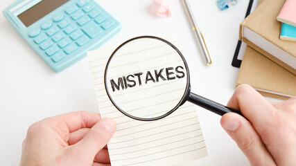 Mistakes text written on paper in hand with magnifying glass on white table