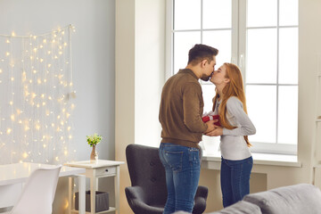 Beautiful young couple at home. Loving couple kissing and enjoying pastime during Valentine's Day celebration with a gift box in hands. Concept of birthday or christmas greetings.