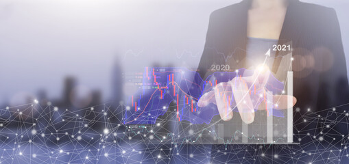 Business growth concept year 2021. Hand touch digital screen hologram growth graph chart sign on city light blurred background. Graph showing the earnings, profits of business shares in good