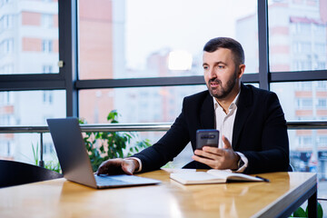 Portrait of a stylish young business man, in a large modern office high on an upper floor, looking into a laptop. Business man at freelancer finance office desk