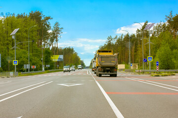 Kiev, Ukraine. May 5, 2021. Cars moving on a paved highway road in the forest, wood with green trees against blue sky at sunny summer or spring day. Truck, cars in motion. Transport, transportation.