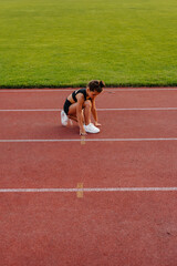 A little girl sat down to tie her shoelaces before running training at the stadium during sunset. Children's sports, and a healthy lifestyle.