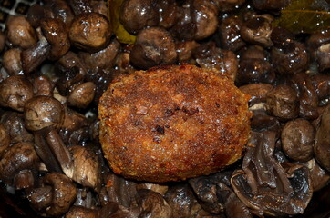 The meat cutlet lies on champignon mushrooms.