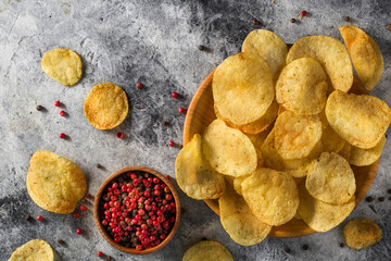 Chips, potato crisps heap with garlic, rosemary, in bowl on grey stone background. Junk food or...