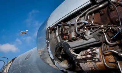 Jet engine exposed with jet flying overhead in the distance