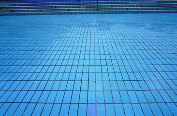 Schwimmbecken ohne Wasser mit blauen Kacheln und Treppenstufen im Schwimmbad im Sommer