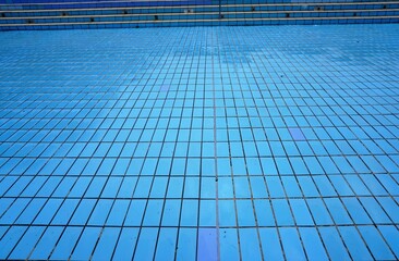 Schwimmbecken ohne Wasser mit blauen Kacheln und Treppenstufen im Schwimmbad im Sommer