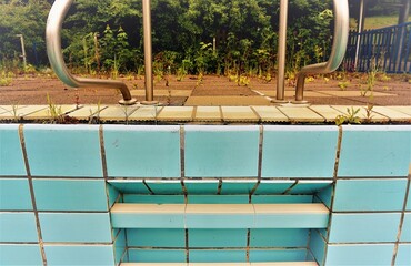 Beckenrand mit Geländer und Treppenstufen eines Schwimmbeckens ohne Wasser im Schwimmbad im Sommer