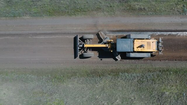 The grader works the lower blade on a rural road. View from above - aerial.