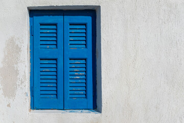 Closed blue shutters on a white wall house in Greece