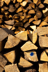 Vorne flacher Holzstapel im Fokus und im Hintergrund hoher Holzstapel aus gehacktem und ordentlich aufgeschichtetem Scheitholz und Kleinholz zum Trocknen für Kaminholz und Brennholz