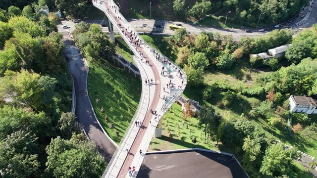 Aerial Top View On Pedestrian Glass Bridge With A Crowd Of Walking People And Red Bike Lanes. Fly Above Bicycle And Pedestrian High Bridge With Glass Sections And Panoramic Views. Drone View