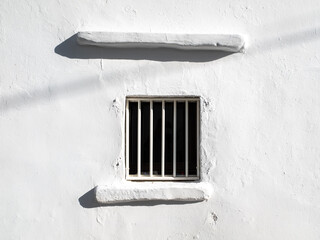 A window with bars on a white wall house in Greece