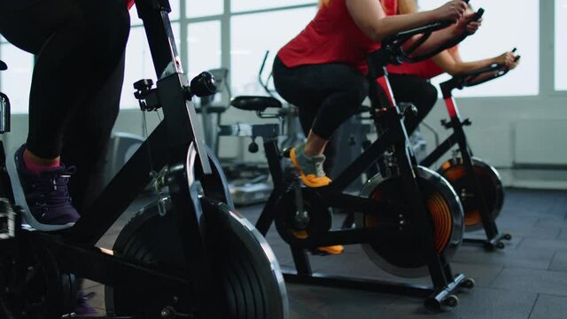 Woman coach engaged spinning on stationary bike with group of people in gym. Athletic girls performing aerobic riding training cycling exercises. Weight Loss Healthy Cardio. Modern active sport indoor