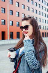Obraz premium young pretty brunette business woman posing emotional against modern building in glasses holding coffee, lifestyle people concept