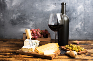 Red wine in a dusty bottle and glass. Grapes and olives with cheese on a wooden table