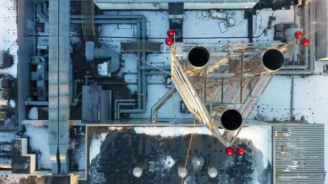 Heating, ventilation and air conditioning systems installed on a snow-covered rooftop. Smoke is coming out of the chrome-plated triple chimney. Aerial top down view