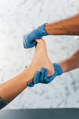 Close up of a podiatrist hands with medical gloves exploring the foot of a patient in the podiatry clinic.