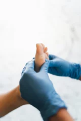 Tuinposter Close up of a podiatrist hands with medical gloves exploring the foot of a patient in the podiatry clinic. © Henko Studio