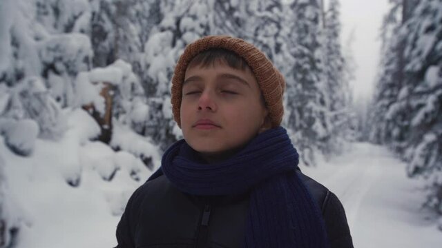 Boy taking deep breaths in the forest in winter. The child with a contemplative gaze in the forest takes a deep breath and gives it back.