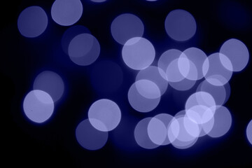 Defocused bokeh lights on black background, an abstract naturally blurred backdrop for Christmas eve or birthday party. Festive light texture. Violet blue garland in blur. Color 2022